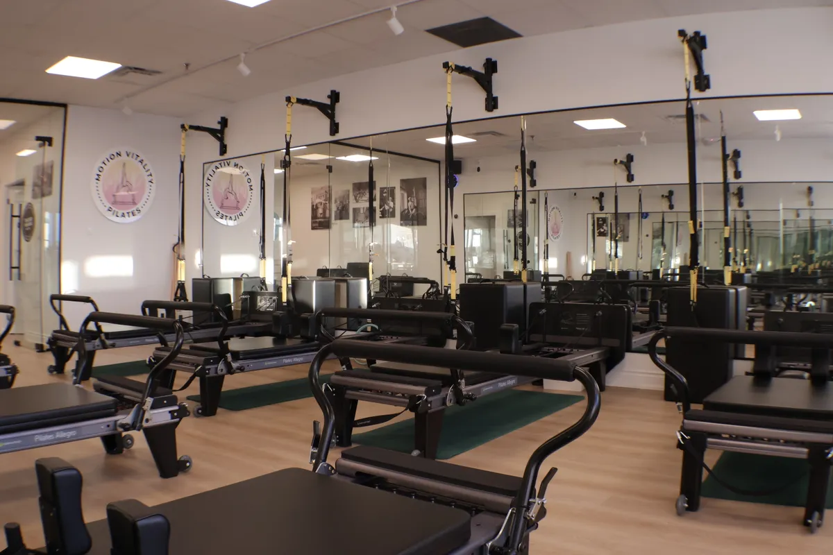 Bright, mirrored reformer studio at Motion Vitality Pilates in Markham, lined with Pilates reformers and TRX straps.
